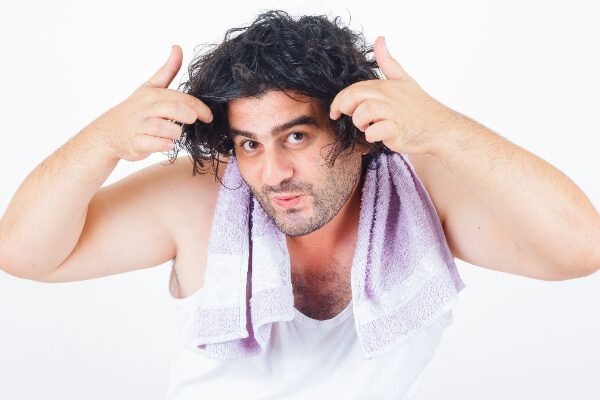 L'uomo fa un'espressione divertente pettinandosi la coda di cavallo e i riccioli con un asciugamano sul collo.