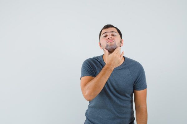 Giovane con la barba che si tocca il collo nel tentativo di esaminare quella zona del corpo.