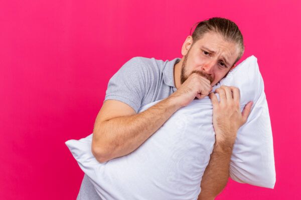 Ragazzo giovane con allergie nasali che mostra insicurezza e stanchezza mentre abbraccia un cuscino con uno sguardo perso.
