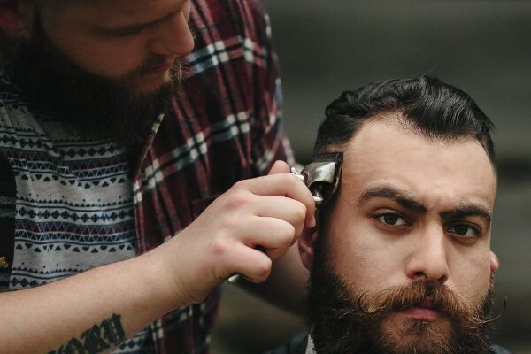 Uomo adulto che riceve il taglio di capelli con un rasoio mentre fissa la telecamera con un'espressione seria.