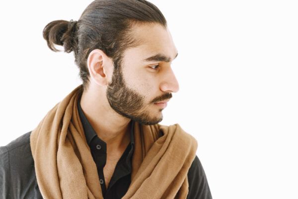 Ragazzo con sciarpa e diverso stile di capelli legati in uno chignon.