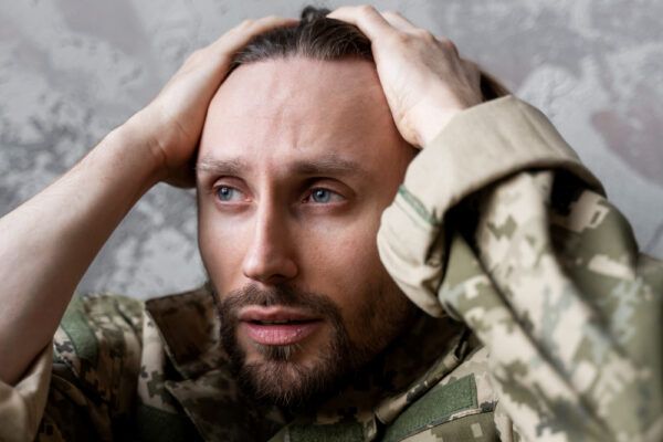 Ragazzo militare con la faccia sporca che si tocca la testa stordito da una situazione.