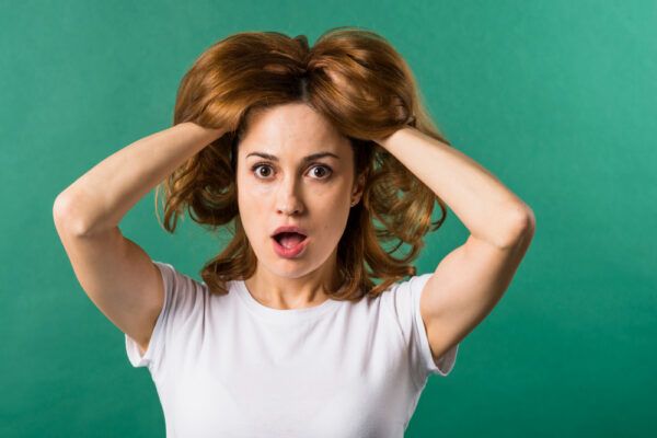 Ragazza con i capelli corti che si tocca il cuoio capelluto e sorpresa mentre guarda la telecamera e posa su uno sfondo verde.