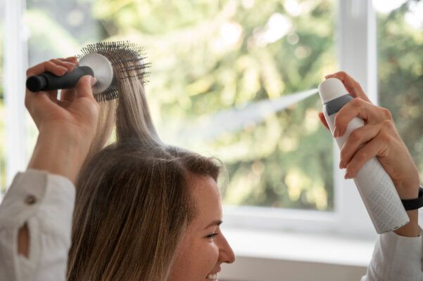 Ragazza dai capelli bionda sorridente che usa lo shampoo secco a casa mentre si lava i capelli.