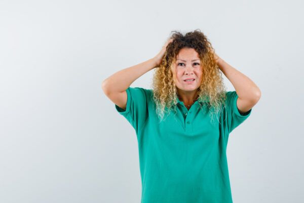 Una signora di mezza età con i capelli ricci tinti di biondo si tocca il cuoio capelluto per il disagio - Alterazioni del cuoio capelluto. 