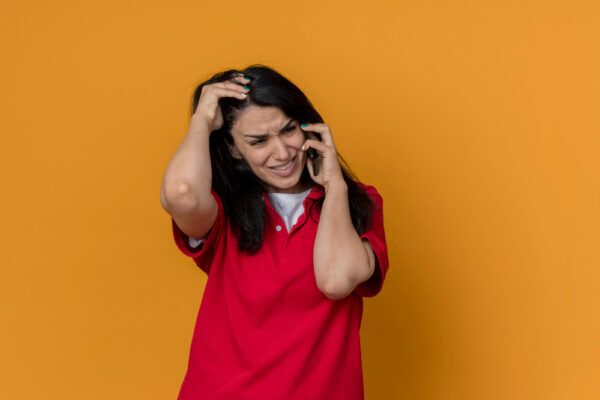 Ragazza in uniforme rossa che parla al telefono mentre si tocca la testa con un'espressione fortemente stressata.