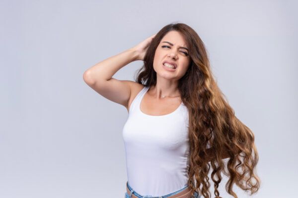 Giovane donna con i capelli lunghi, una mano sulla testa, che guarda di lato con un'espressione lamentosa.