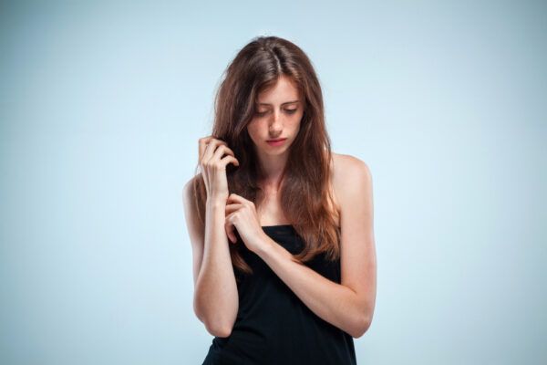 Una ragazza con i capelli lunghi e spettinati soffre e ha il viso abbassato.