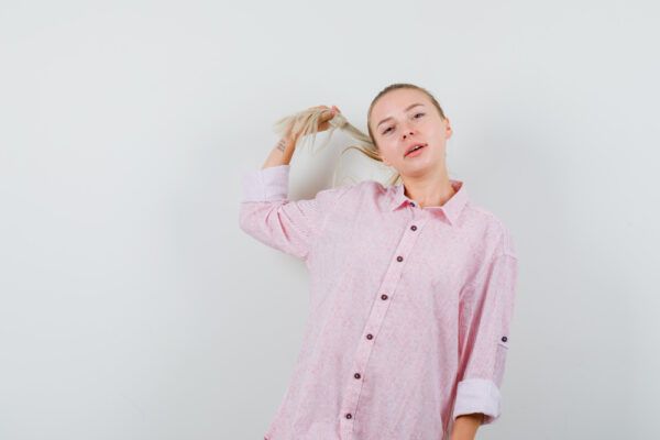 Ragazza con una camicia rosa che prende una ciocca di capelli gialli con la mano - Capelli vittima di sbilancio ormonale.