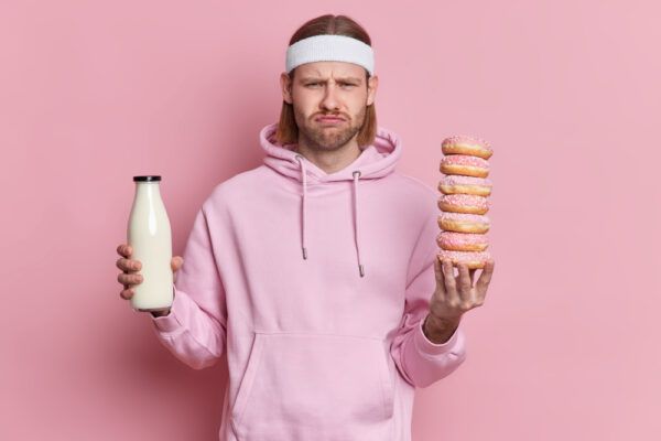 Ragazzo con la faccia sconvolta mentre usa una fascia per esercizi e tiene alcune ciambelle in mano e una bottiglia di latte nell'altra.