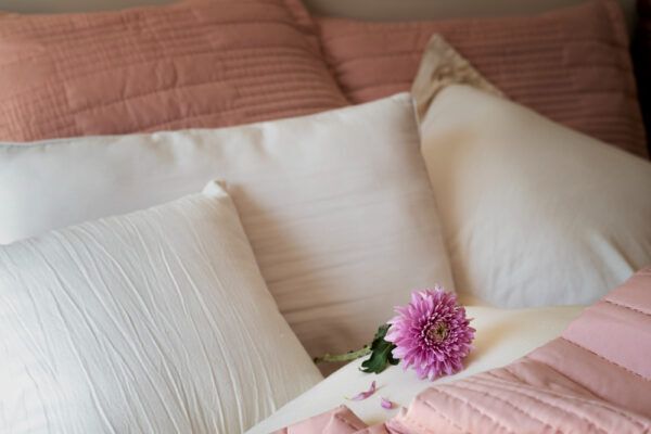 Letto preparato con comodi cuscini di diverse dimensioni e colori, con un fiore davanti.