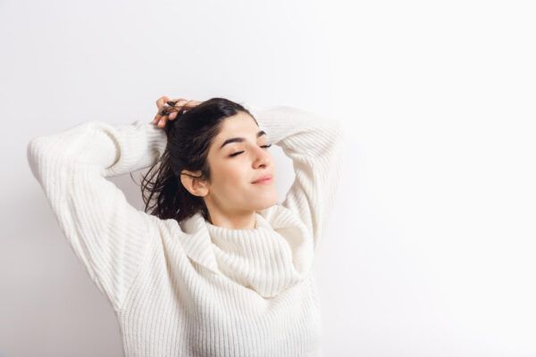 Ragazza in maglione bianco che sorride con gli occhi chiusi mentre si tocca i capelli con soddisfazione.