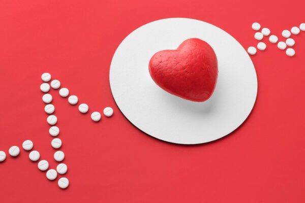 Sfondo rosso con pillole che segnano la frequenza cardiaca e termina con un cuore.