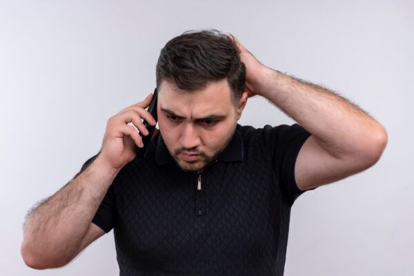 Un giovane ragazzo dai capelli castani parla al telefono mentre si tocca il cuoio capelluto con aria preoccupata - Problemi capillari diversi.