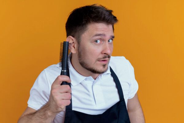 Barbiere con grembiule nero che tiene in mano una spazzola per pettinarsi.