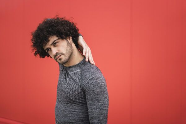 Un giovane con i capelli ricci e secchi si tocca la schiena con la mano in posizione di stretching a causa del disagio.