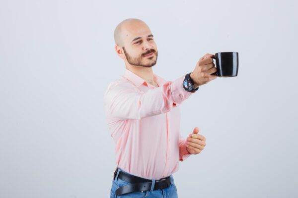 Uomo calvo in camicia abbottonata con il braccio teso mentre tiene una tazza di caffè in mano.