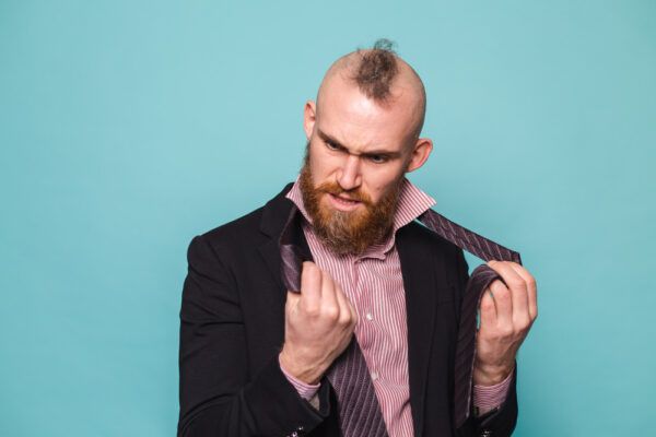 Uomo crestato in abito formale e cravatta che si guarda le mani con espressione confusa.
