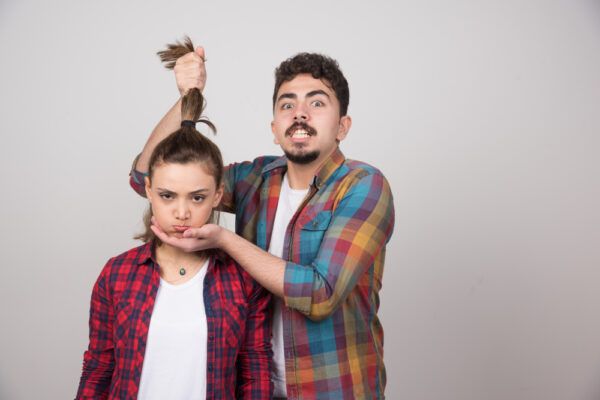 Ragazzo che tiene la coda di cavallo di una giovane donna infastidita mentre lei ha un'espressione scontenta.