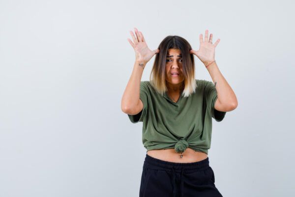 Donna con i capelli corti con punte gialle e un corpo grosso che posa con un'espressione sbalordita davanti alla telecamera.
