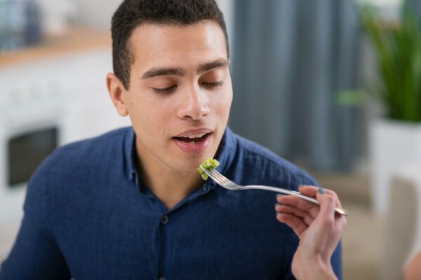 Giovane ragazzo che riceve un morso di verdure in bocca.