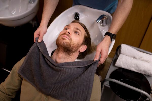 Ragazzo sdraiato su un lavandino mentre si lava i capelli - Ossigenoterapia per infoltire i capelli.