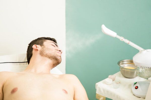 Uomo sdraiato su una barella che riceve vapore sul viso mentre frequenta una spa.