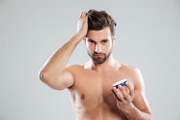bell'uomo con una mano tra i capelli e l'altra che tiene un contenitore di crema