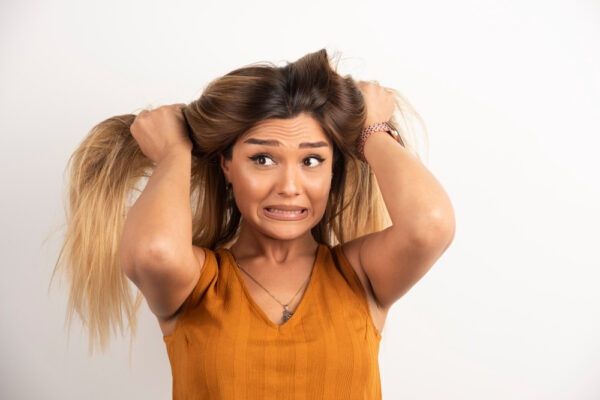 Ragazza carina con i capelli biondi che si tiene i capelli mentre fa una smorfia con il viso.