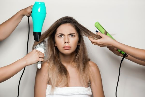 Una donna preoccupata si asciuga i capelli con un asciugacapelli, una piastra e una spazzola.
